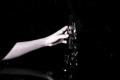 Monochrome image of a hand delicately holding a multifaceted glass sculpture, likely crystal. Strong contrast emphasizes form...