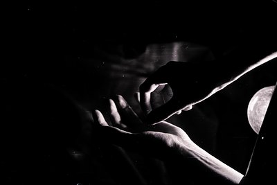 Close-up, high-contrast image shows two hands forming a heart shape against a dark backdrop. Strong directional light creates...