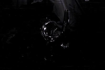 Striking black and white image featuring a highly reflective, stylized metal sphere suspended in darkness. Hints of blurred b...