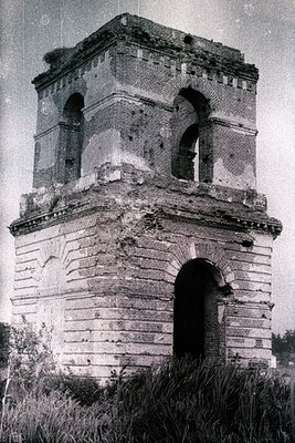 Eroded, two-story brick structure with arched windows, displaying signs of weathering & possible damage. Architectural style ...