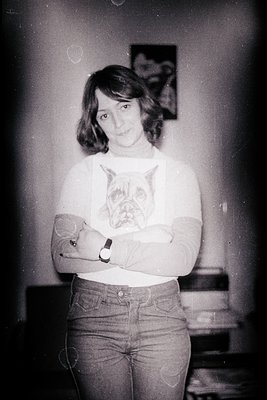 A young woman stands with arms crossed, wearing a graphic tee featuring a bulldog design and tight jeans. The photo, likely t...