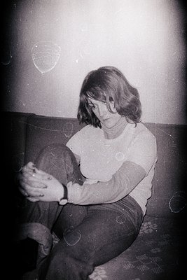 Seated woman with short, dark hair examines a small, folded object in her hands. Casual attire - likely a t-shirt and dark tr...