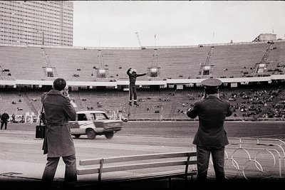 A male athlete, mid-air during a high jump competition, dominates the scene against a backdrop of a large stadium and a high-...