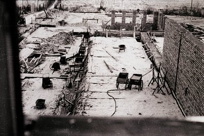Black-and-white aerial view of a mid-20th-century construction site with exposed trenches, wooden scaffolding, and a horse-dr...