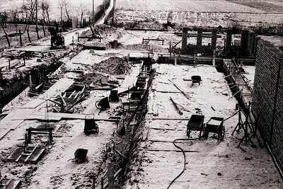 Aerial view of a heavily damaged industrial site, likely post-war. Ruined brick structures, collapsed machinery, and scattere...