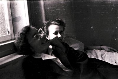 Intimate black-and-white portrait of two individuals sharing a moment indoors, likely mid-20th century. The man leans in to k...