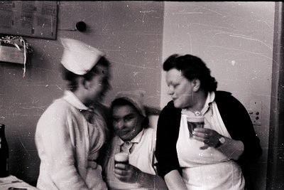 Three women in 1950s-60s medical uniforms—nurse caps, starched collars—stand indoors, holding glasses. Blurred faces suggest ...