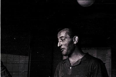 Black-and-white portrait of a man in a dark, textured shirt, captured in low-light with a grainy, vintage filter. His express...