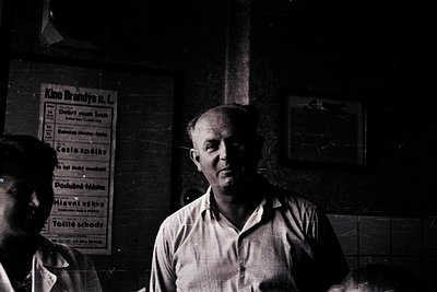 Mid-20th century black-and-white portrait of a man in a light button-down shirt, standing indoors beside a Kino Brandýs cinem...