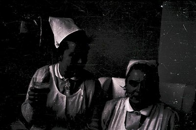Vintage sepia-toned portrait of two men in early 20th-century attire, likely 1910s–1920s. The man on left wears a peaked cap ...