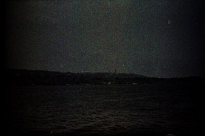 Nighttime coastal scene with faint horizon line separating dark water from a star-studded sky. Milky Way galaxy faintly visib...