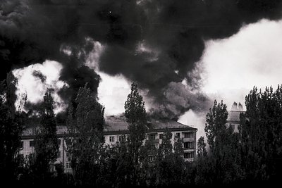 Dramatic black-and-white shot of dense smoke obscuring mid-20th-century apartment blocks, likely Eastern European. Multi-stor...