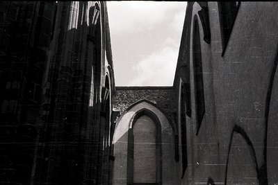 Gothic-style arched doorway framed by angular, reflective stone walls. Dramatic play of light and shadow emphasizes architect...