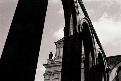Black-and-white architectural detail featuring a grand archway with intricate stone carvings and classical columns. Partial v...