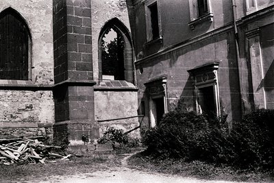 Black-and-white photograph of a weathered Gothic Revival church exterior, featuring pointed arches and ornate stonework. Stac...