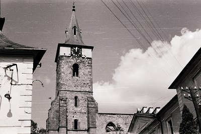 Historic stone church tower with round clock face, steeply pitched roof, and arched buttresses. Mid-20th century urban archit...