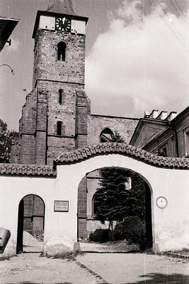 Historic stone church tower with arched entrance gate, likely Eastern European architecture. Clock face visible on tower. Sig...