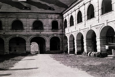 Historic courtyard with arched stone cloister, likely European monastic or institutional architecture. Symmetrical arcades wi...