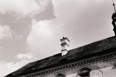 Classic black-and-white shot of a European-style chimney atop a tiled roof, framed by dramatic storm clouds. Architectural de...