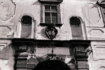 Classic Baroque façade featuring ornate stonework, two arched windows with decorative keystones, and a central relief sculptu...