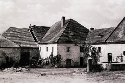 Rural farmstead featuring weathered stone and timber-framed buildings with steep gable roofs, likely European. Central struct...