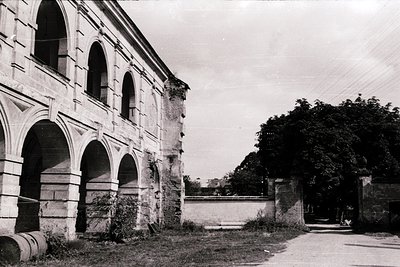Neoclassical stone building with arched colonnades, showing signs of aging and weathering. Likely a public or institutional s...