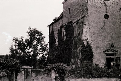 Vintage black-and-white shot of a weathered stone building with ivy-covered walls and a small arched entrance. Architectural ...