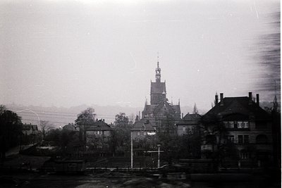 Mid-20th century black-and-white shot of a European town hall with Gothic Revival architecture—steeple, ornate gables, and sy...