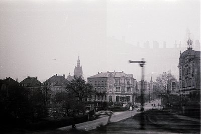 Vintage black-and-white street scene featuring early 20th-century European architecture. Prominent multi-story buildings with...