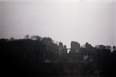 Vintage black-and-white shot of a misty, forested landscape with rocky outcrops. Soft focus and grainy texture suggest early ...