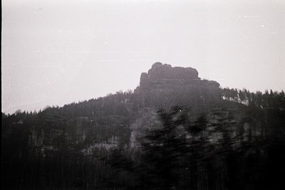Vintage black-and-white shot of a rocky mountain peak with dense forest below, l...