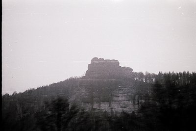 Vintage black-and-white shot of a rugged sandstone rock formation rising from dense forest. Likely Saxony, Germany’s Elbe San...