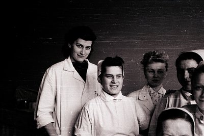 Black-and-white group portrait of five individuals in 1950s-era medical scrubs, likely nurses or medical students. The centra...