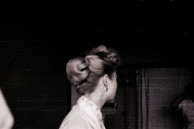 Vintage black-and-white portrait of a woman with an updo hairstyle, likely mid-20th century. She wears a high-necked blouse a...
