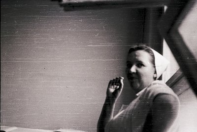 Vintage black-and-white portrait of a man in mid-speech, likely mid-20th century. He stands indoors near a window with visibl...
