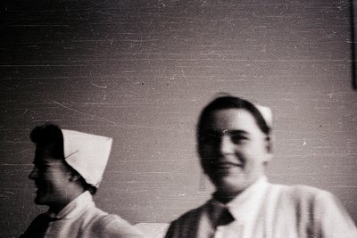 Vintage sepia-toned portrait of two individuals in medical attire, likely nurses, mid-20th century. The man wears a white coa...