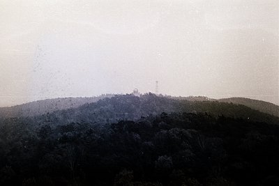Vintage black-and-white aerial view of a hilltop structure amid dense forest, likely a Cold War-era observation tower or rada...