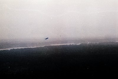 Vintage aerial view of a river winding through dense forest, likely mid-20th century. A lone aircraft hovers above, possibly ...