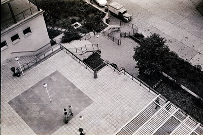 Aerial view of a mid-20th-century urban courtyard with concrete basketball court, metal railings, and minimalist architecture...