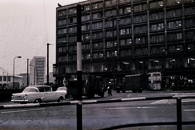 Vintage urban street scene featuring a high-rise Brutalist-style apartment block with exposed concrete and uniform balconies....