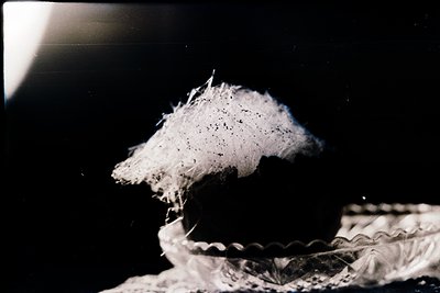 Vintage sepia-toned close-up of a frothy, layered dessert—likely a soufflé—collapsing into a decorative cake dish. Art Deco-s...