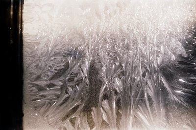 Close-up of frost patterns on a windowpane, showcasing intricate crystalline formations. Likely captured indoors during winte...