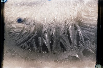 Vintage close-up of crystalline ice formations on a window, likely captured with early film. Sharp, geometric patterns sugges...