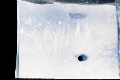 Close-up of a damaged or aged photographic negative showing abstract light leaks and scratches. The central dark spot resembl...