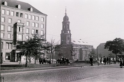 Black-and-white street scene featuring a prominent **19th-century church** with a tall steeple and clock, flanked by **multi-...