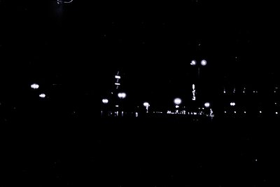 Low-contrast nighttime cityscape with silhouetted buildings and streetlights. Blurred urban lights suggest motion or low-reso...