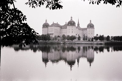 Symmetrical Baroque palace reflected in a serene lake, framed by overhanging foliage. Likely **Marienborg Palace, Denmark**, ...