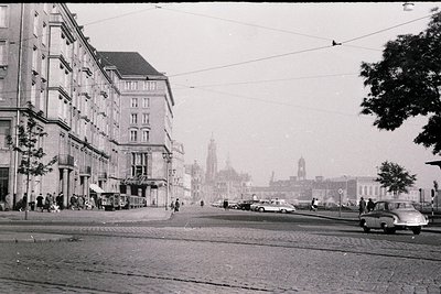 Mid-20th century urban street scene featuring classic European architecture. Prominent multi-story apartment buildings with b...