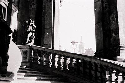 Neoclassical balcony featuring ornate balustrade with sculptural figures in relief. Black-and-white photograph captures grand...