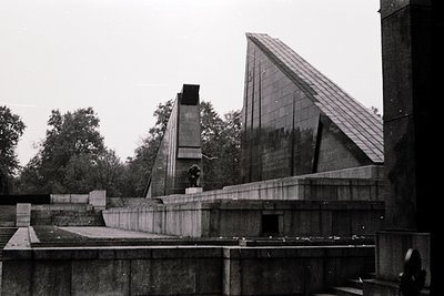 Modernist concrete memorial with geometric, angular design—likely a war or labor monument. Central statue of a figure in cont...